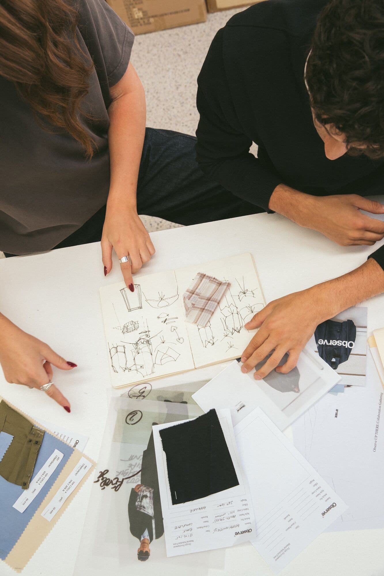 Hands reviewing styling sketches and fabric swatches around a planning table