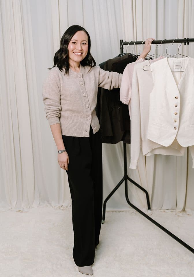 Gulinka, Melbourne personal stylist, standing beside a clothing rail of neutral-toned pieces