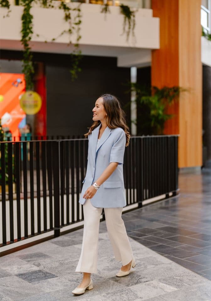 Gulinka smiling outside a store entrance in a pale blue blazer