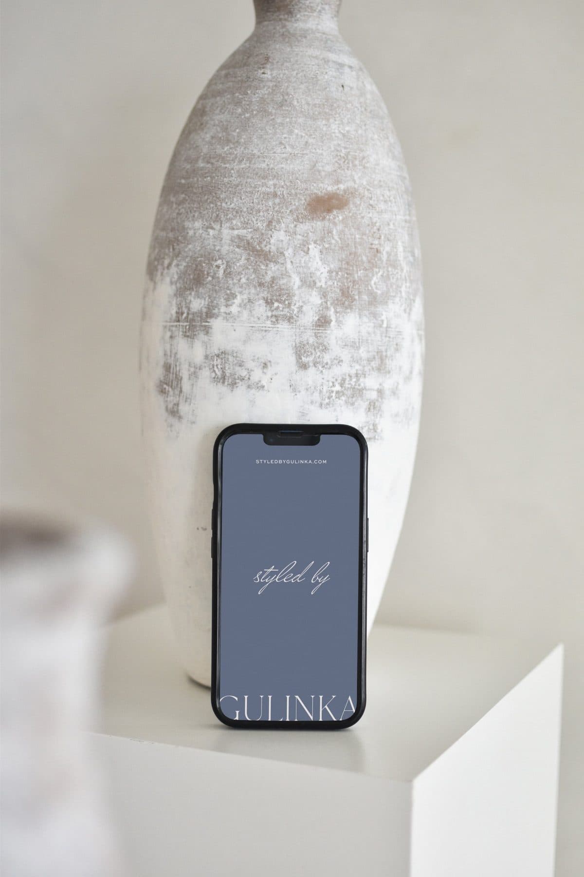 "styled by GULINKA" logo on a phone screen beside a white ceramic vase