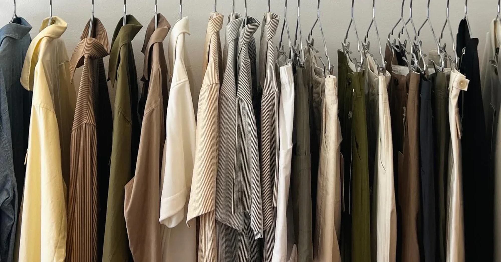 A rail of shirts, knits and trousers in a sunlit studio