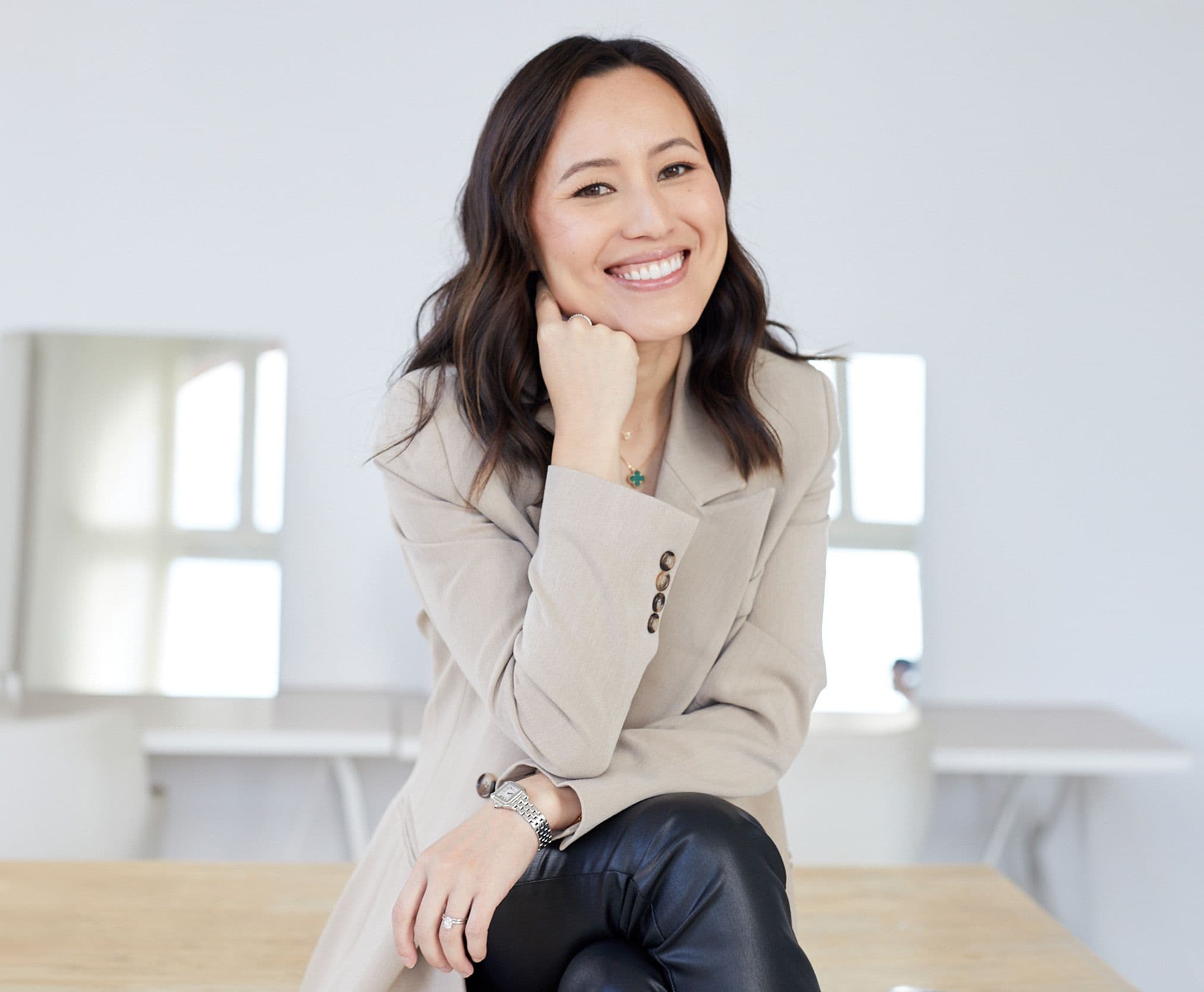 Gulinka seated in a beige blazer, smiling with her chin resting on her hand