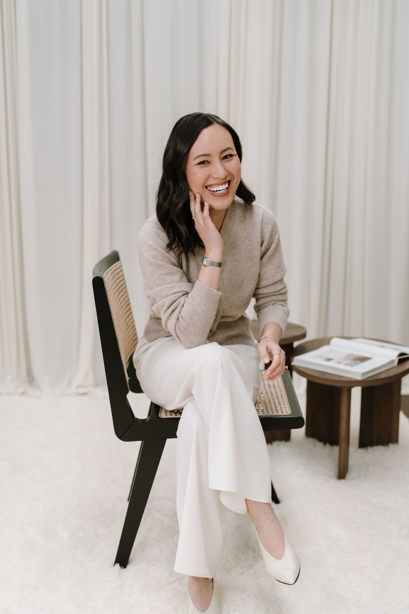 Gulinka seated on a cane chair, laughing, in white trousers